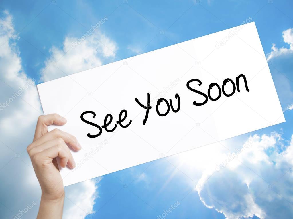 See You Soon Sign on white paper. Man Hand Holding Paper with text. Isolated on sky background.  Business concept. Stock Photo