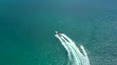 Tropikal turkuaz körfezde yüksek hızda seyreden sürat teknesi donut su sporlarının insansız hava aracı fotoğrafı. Tayland, Phuket, Kata Sahili