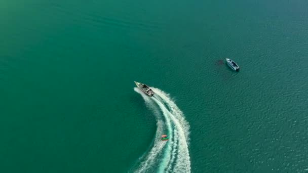 Foto aérea drone de barco a motor extremo donut água-esportes cruzeiro em alta velocidade na baía de turquesa tropical. Tailândia, Phuket, praia de Kata — Vídeo de Stock