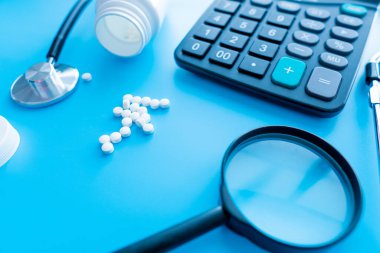 İlaç ve haplar büyüteç altında tıbbi bir steteskopun yanında. Sağlık konsepti ve ilaçların, vitaminlerin ve çeşitli takviyelerin sorumlu kullanımı