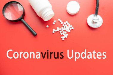 Stetoskop, kırmızı zemin üzerinde CORONAVIRUS UPDATES yazan büyüteç. Covid-19 konsepti ve koronavirüs