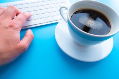 Çalışma masasının yaratıcı düz yatay fotoğrafı. Mavi arka planda klavyesi ve kahve fincanı olan üst görünüm ofis masası..