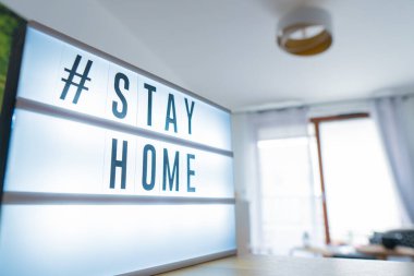 Coronavirus ev tabelasının üzerinde # STAYHOME etiketi olan ışıklı ışık kutusu. COVID-19 afişi evde kalarak kendini izole etmeyi teşvik ediyor. Daire arkaplanı