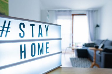 Coronavirus ev tabelasının üzerinde # STAYHOME etiketi olan ışıklı ışık kutusu. COVID-19 afişi evde kalarak kendini izole etmeyi teşvik ediyor. Daire arkaplanı