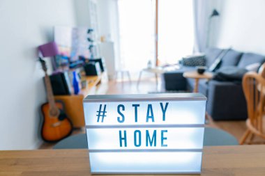 Coronavirus ev tabelasının üzerinde # STAYHOME etiketi olan ışıklı ışık kutusu. COVID-19 afişi evde kalarak kendini izole etmeyi teşvik ediyor. Daire arkaplanı