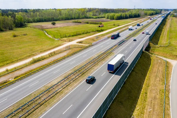 Cars and freight semi truck driving on busy highway across the country in beautiful summer evening. People on road trip traveling on busy freeway at golden sunset