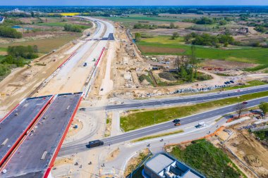 Havadan aşağıya, bitmemiş asfalt yol manzaralı, inşaat alanında ağır makineler var. Hiçliğe giden yol.