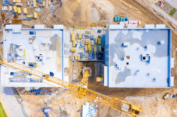 Aerial view of tower lifting crane and concrete frame of tall apartment residential building under construction in a city. Urban development and real estate growth concept.