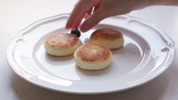 Kvinna lägger blåbär på tallriken med ost pannkakor — Stockvideo