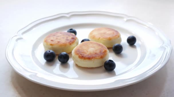 Woman puts honey on the plate with cheese pancakes served with fresh blueberries — Stock Video