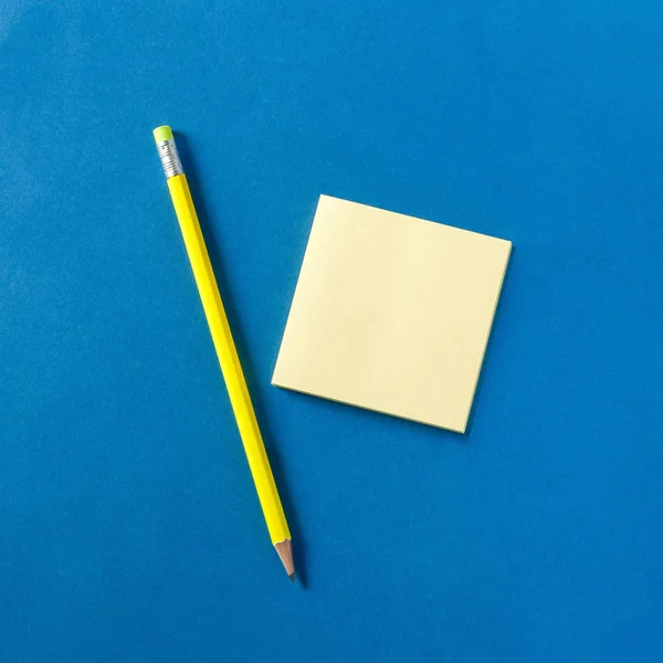 Lápis amarelo néon e bloco de notas em fundo azul, vista superior — Fotografia de Stock