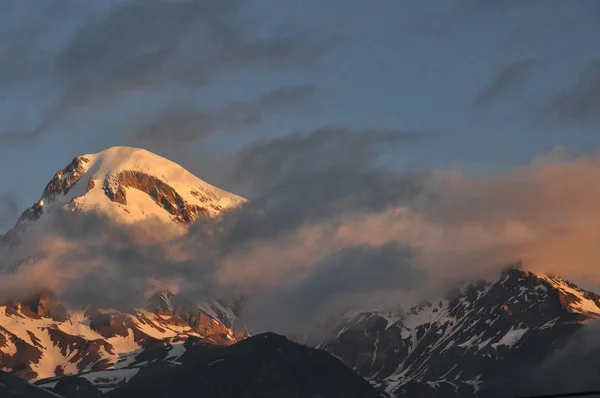 Schneebedeckte Berge kasbek in der Morgendämmerung und das Tal unten, wo es eine Kirche siete trinity. Georgien. — Stockfoto