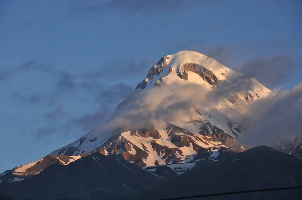Schneebedeckte Berge kasbek in der Morgendämmerung und das Tal unten, wo es eine Kirche siete trinity. Georgien. — Stockfoto