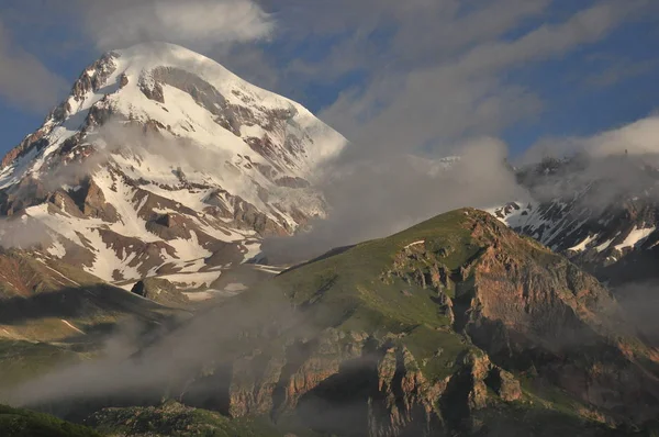 Besneeuwde bergen Kazbek bij dageraad en de vallei hieronder waar is er een kerk siete Trinity. Georgië. — Stockfoto