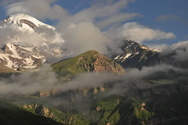 Montagne innevate Kazbek all'alba e la valle sottostante dove si trova una chiesa siete Trinità. Georgia . — Foto Stock