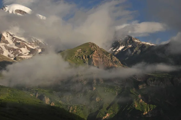 Schneebedeckte Berge kasbek in der Morgendämmerung und das Tal unten, wo es eine Kirche siete trinity. Georgien. — Stockfoto