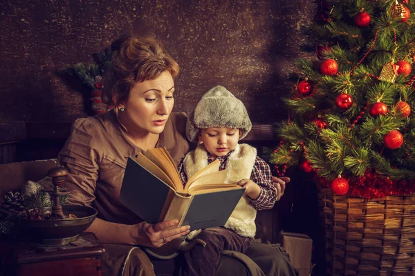 Moeder leest aan zijn zoon het boek in de buurt van een kerstboom. — Stockfoto