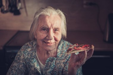 Çok yaşlı kadın evde bir parça pizza yemek.