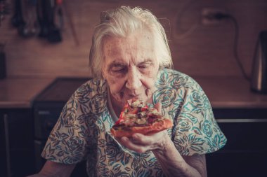 Çok yaşlı kadın evde bir parça pizza yemek.