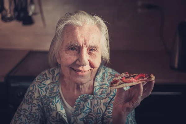 Mulher muito idosa comendo um pedaço de pizza em casa . — Fotografia de Stock