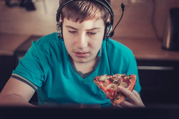 Teenager eating pizza sitting at a laptop.