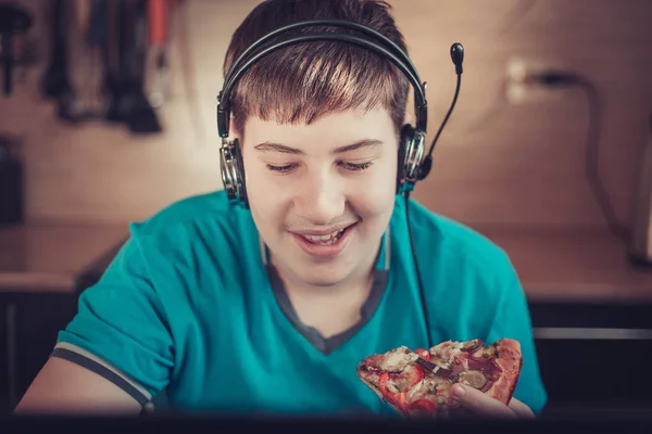 Tiener eten pizza zit op een laptop. — Stockfoto
