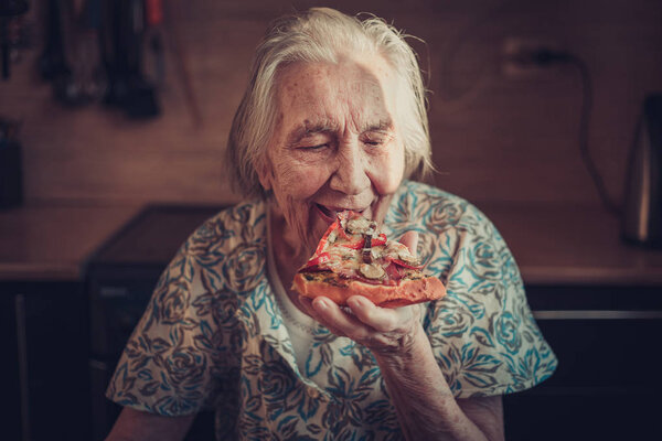 Very elderly woman eating a piece of pizza at home.