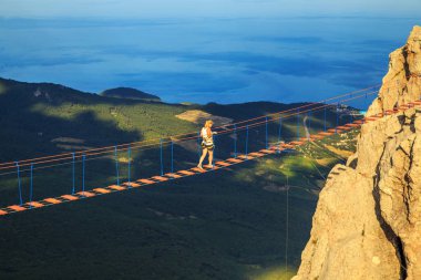 Kadın bir uçurumun üzerinde bir asma köprü yürüyor.
