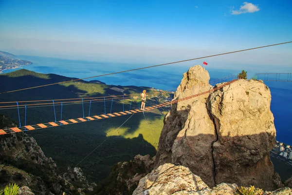 Kadın bir uçurumun üzerinde bir asma köprü yürüyor.