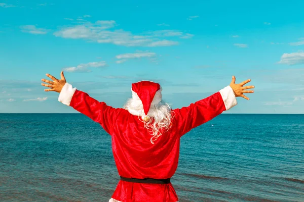 Père Noël est debout sur la plage avec les bras tendus . — Photo