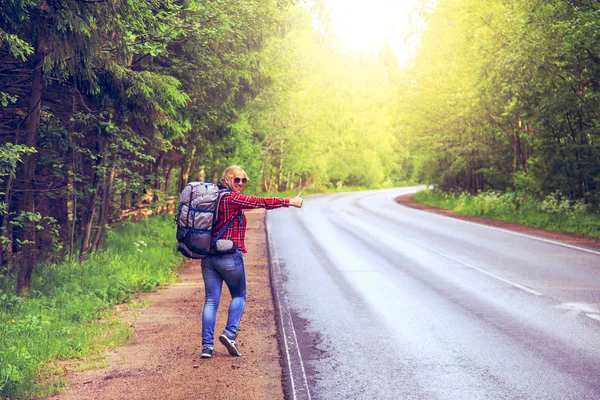 Menina solitária carona na estrada com uma mochila . — Fotografia de Stock