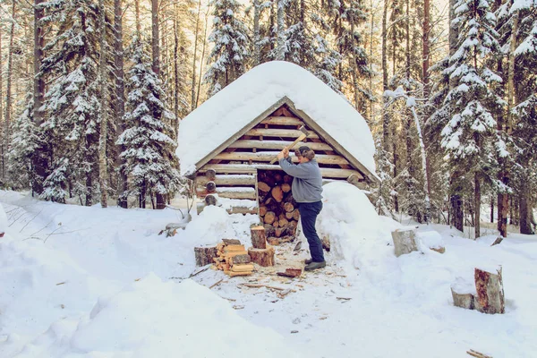 Mann hackt Holz im Wald in der Nähe der Hütte. — Stockfoto