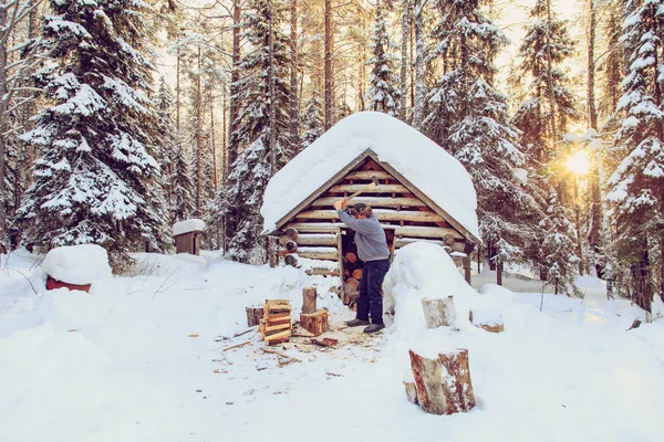 Mann hackt Holz im Wald in der Nähe der Hütte. — Stockfoto