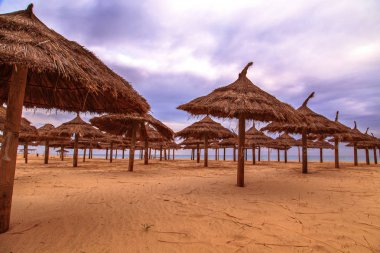 Bulutlu bir günde sahilde hasır şemsiyeler.