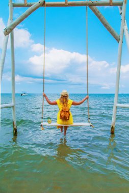 Sarı elbiseli bir genç kadın salıncakta oturuyor.