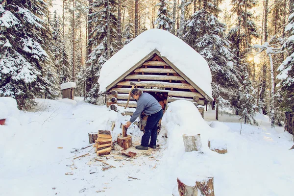 Mann hackt Holz im Wald in der Nähe der Hütte. — Stockfoto