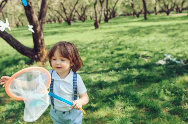 mutlu yürümeye başlayan çocuk bahçesinde bahar yürüyüşte net kelebekler yakalamak. Mevsimlik açık hava etkinlikleri. 