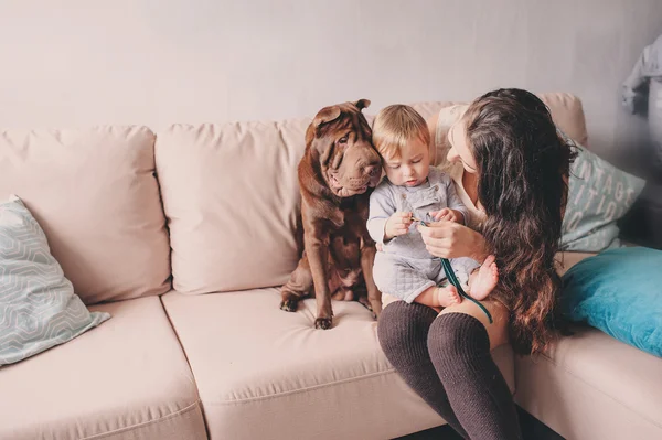 Happy mother and baby son playing together at home with cute shar pei dog. Cozy indoor lifestyle scene — Stock Photo, Image