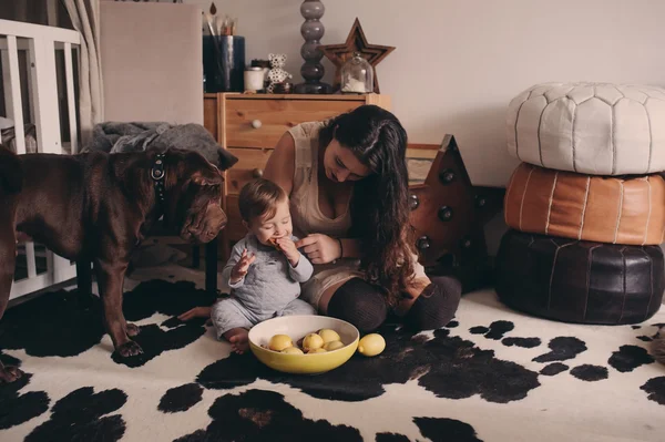Famille heureuse jouant à la maison avec chien. Mère et bébé garçon mangeant des biscuits et passant du temps ensemble — Photo