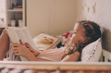 kız yatakta oturuyor ve onun odasına kitap okuma ufaklık. Sıcak hafta sonu evde, yaşam tarzı yakalama