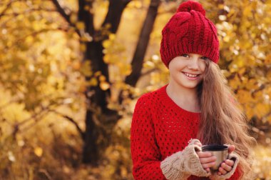 mutlu çocuk kız sıcak kırmızı örgü şapka ve atkı üzerinde sıcak sonbahar sıcak çay içme termos yürümek. Mevsimlik açık hava etkinlikleri