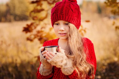mutlu çocuk kız sıcak kırmızı örgü şapka ve atkı üzerinde sıcak sonbahar sıcak çay içme termos yürümek. Mevsimlik açık hava etkinlikleri