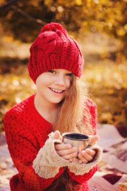 mutlu çocuk kız sıcak kırmızı örgü şapka ve atkı üzerinde sıcak sonbahar sıcak çay içme termos yürümek. Mevsimlik açık hava etkinlikleri