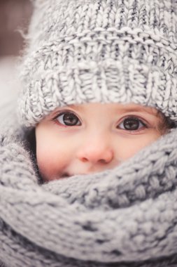 winter portrait of beautiful baby girl in warm oversize knitted scarf and hat on the walk in snowy winter forest clipart