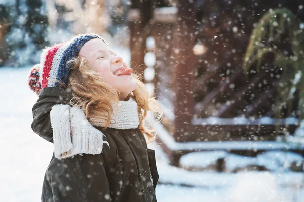 Happy child girl catching snowflakes and playing on winter snowy walk in garden, seasonal outdoor activities on vacations — Stock Photo, Image