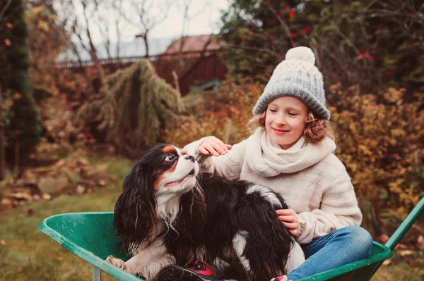 Glad rolig barn flicka rider hennes hund i skottkärra i höst trädgård, uppriktig utomhus capture, barn som leker med husdjur — Stockfoto