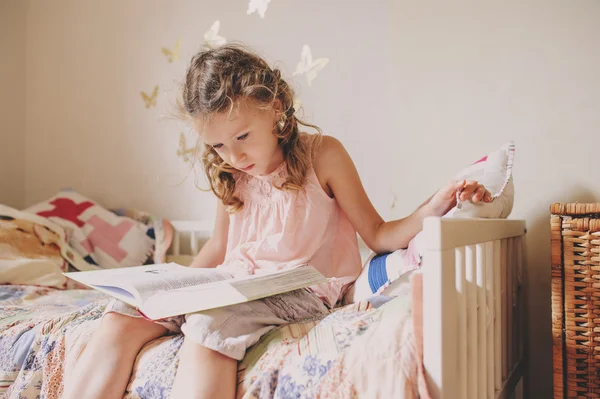 Dziecko dziewczynka siedzi na łóżku i czytanie książki w jej pokoju. Przytulne weekend w domu, styl życia przechwytywania — Zdjęcie stockowe