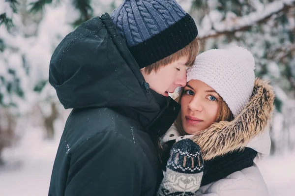 Giovane coppia felice passeggiando nella foresta innevata invernale, indossando caldi guanti a maglia con ornamento natalizio — Foto Stock