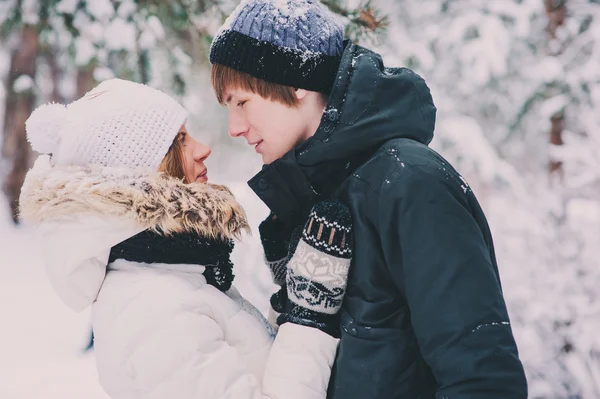 Молодая счастливая пара, гуляющая зимой в снежном лесу, в теплых вязаных перчатках с рождественским орнаментом — стоковое фото