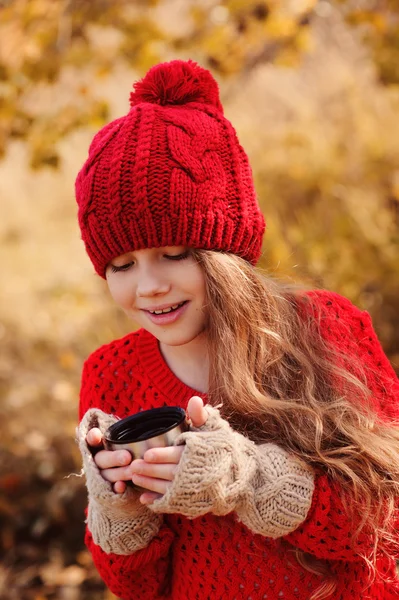 快乐的孩子女孩在暖红色针织的帽和围巾上舒适的秋天从热水瓶走喝热茶。季节性的户外活动 — 图库照片